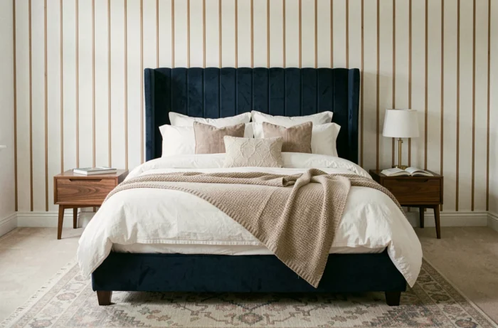Lit king size avec tête de lit en velours bleu marine et literie en lin blanc dans une chambre élégante aux boiseries en chêne
